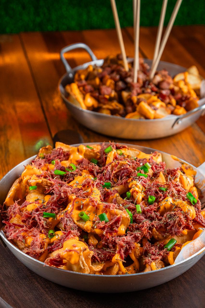 Batata frita carregada coberta com molho de queijo cheddar, carne desfiada e cebolinha